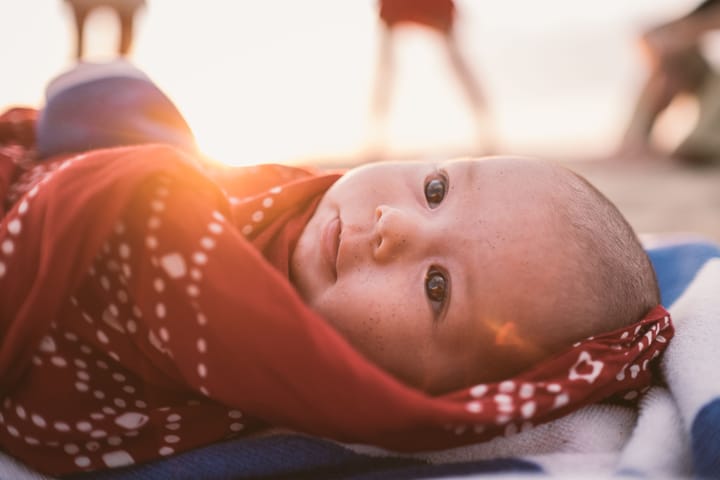 a baby wrapped in a beautiful red shawl with a warm sunset in the background.